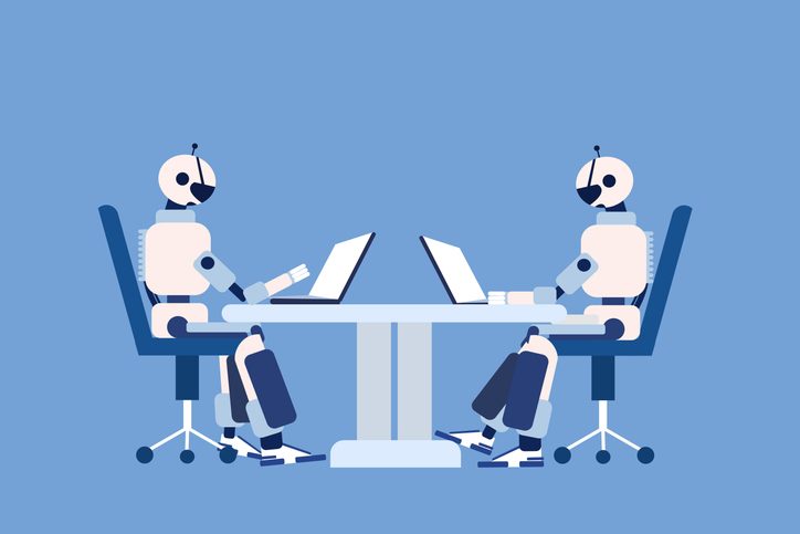 Two robots sitting on chairs and working on their laptops for article on